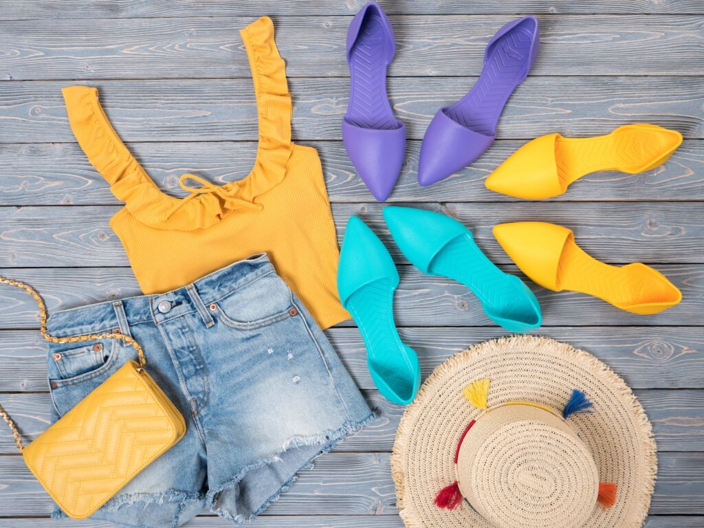 Womens clothing, accessories, shoes (yellow top, denim shorts, crossbody bag, straw hat, flat sandals). Fashion outfit, spring summer collection. Shopping concept. Flat lay, view from above Freedom of beach